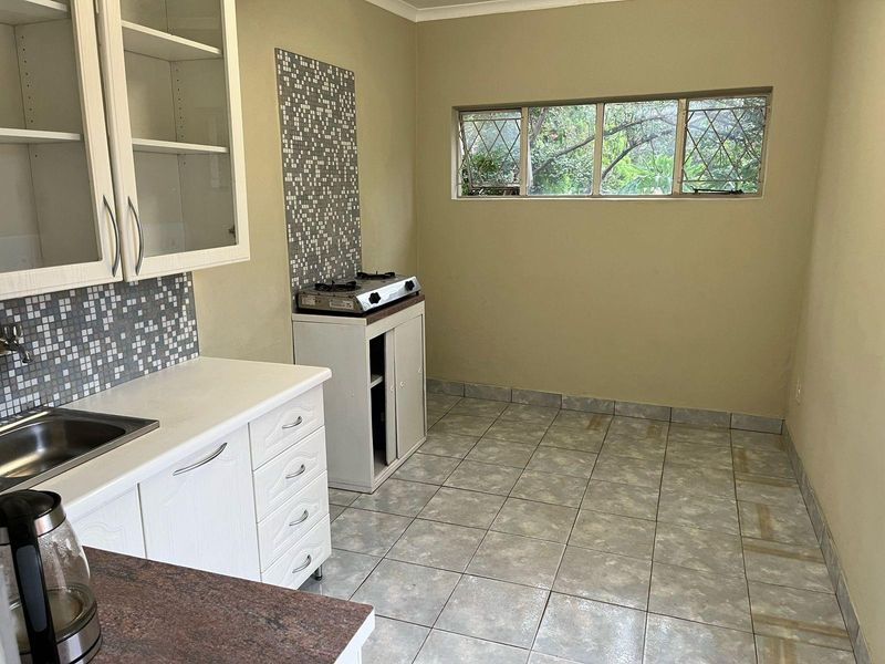A functional kitchen space featuring white cabinetry, tiled splashbacks, a gas cooktop, and tiled flooring, offering a blank canvas for potential renovation.
