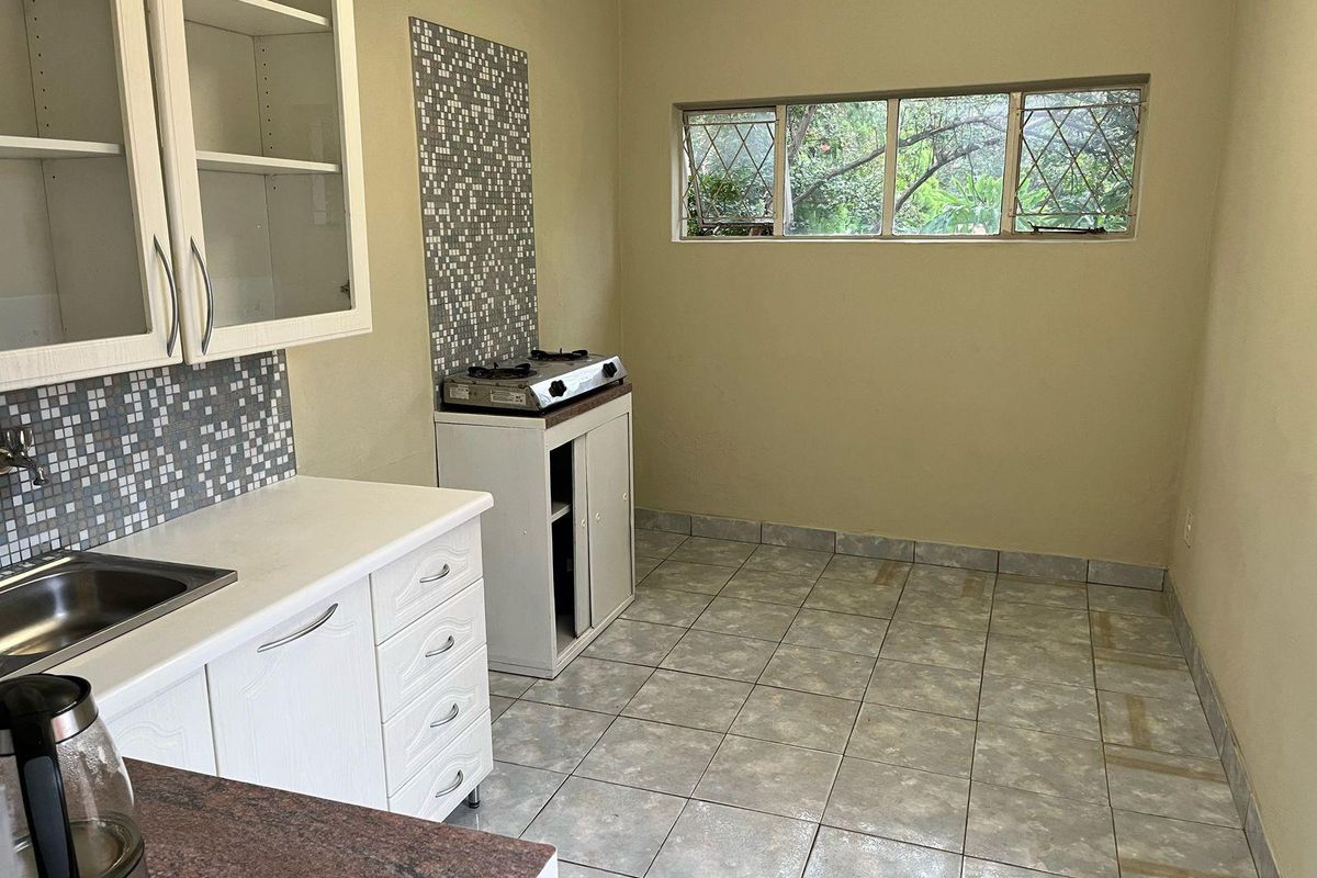 A functional kitchen space featuring white cabinetry, tiled splashbacks, a gas cooktop, and tiled flooring, offering a blank canvas for potential renovation.