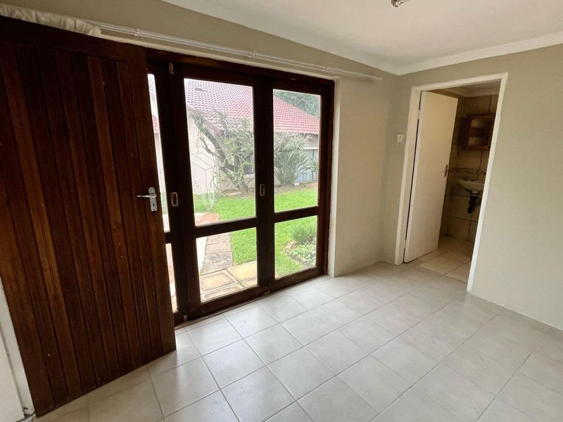 An empty living area featuring neutral tiled flooring and timber-framed glass doors providing direct access to the garden.