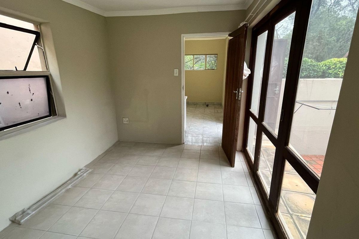 An empty, tiled living area featuring large timber-framed glass doors providing access to the exterior, with neutral walls and coved cornicing.