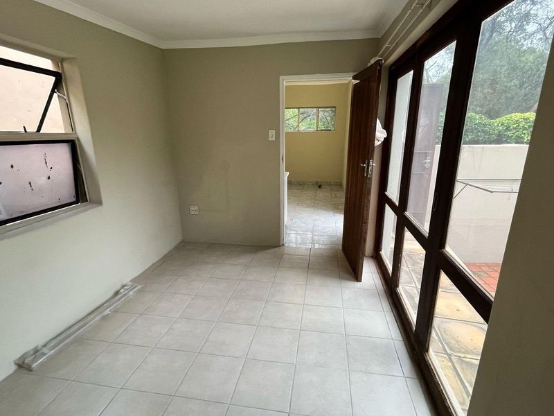 An empty, tiled living area featuring large timber-framed glass doors providing access to the exterior, with neutral walls and coved cornicing.