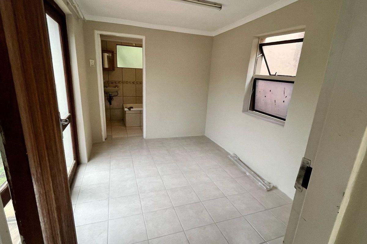 An empty bedroom featuring tiled flooring, a top-hung window, and an en-suite bathroom access point.