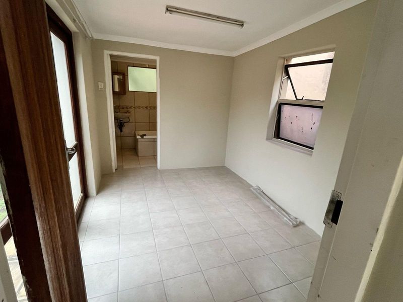 An empty bedroom featuring tiled flooring, a top-hung window, and an en-suite bathroom access point.