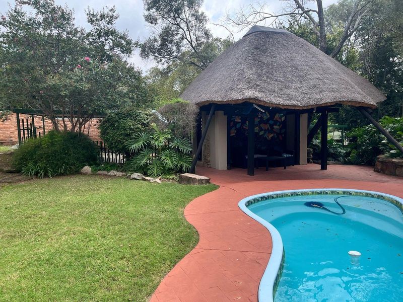 Outdoor entertainment area featuring a swimming pool and a traditional thatched lapa set within a landscaped garden.