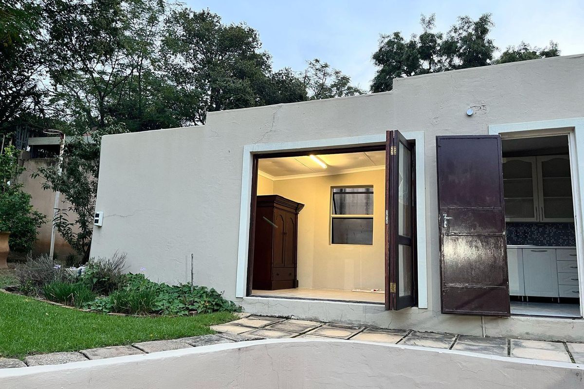 Rear view of the cottage featuring a paved walkway, stepped parapet wall, and direct access to the interior living space through timber doors.