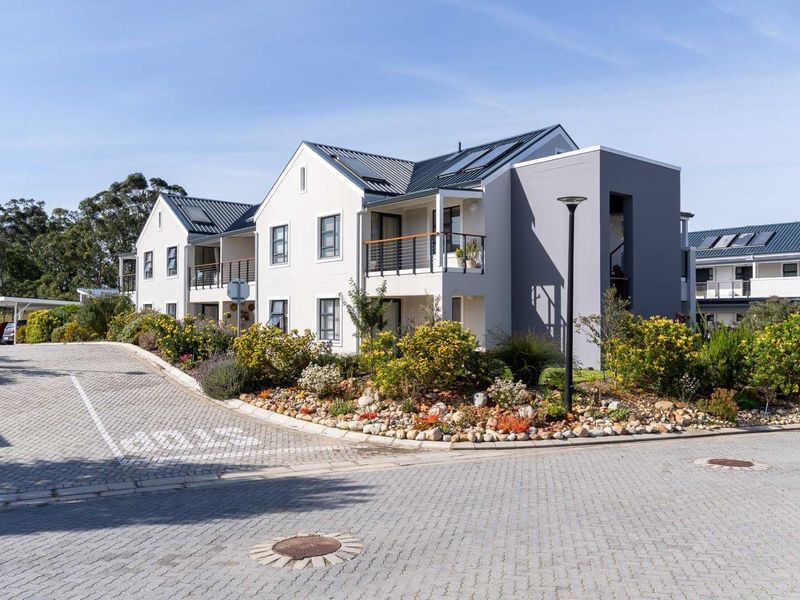 Modern apartment complex featuring a paved driveway, landscaped garden, and balconies with metal roofing and integrated solar panels.