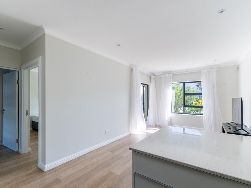Bright and spacious open-plan living area featuring modern laminate flooring, recessed lighting, and a sleek stone-topped kitchen island with access to outdoor views.
