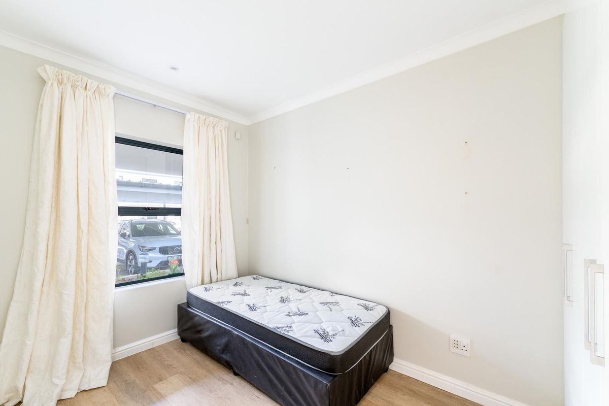 A bedroom featuring laminate flooring, a built-in wardrobe, and a window with curtains, providing a neutral space ready for personalization.