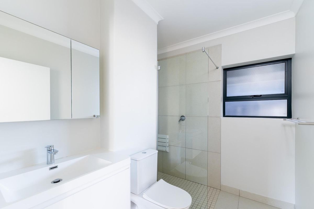 Modern, clean-lined bathroom featuring a vanity with integrated basin, mirror cabinet, toilet, and a walk-in shower with a glass screen.
