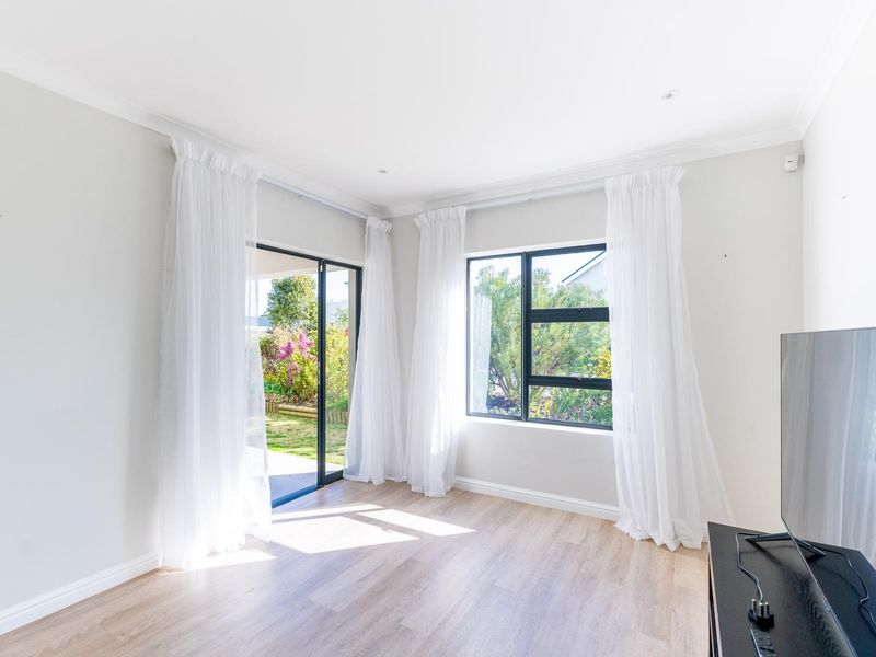 Bright and airy living room featuring modern laminate flooring, large windows, and a sliding glass door providing direct access to the garden.