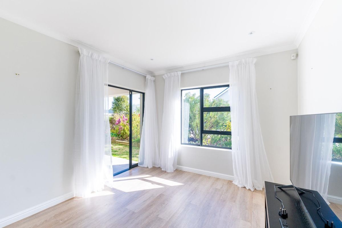Bright and airy living room featuring modern laminate flooring, large windows, and a sliding glass door providing direct access to the garden.