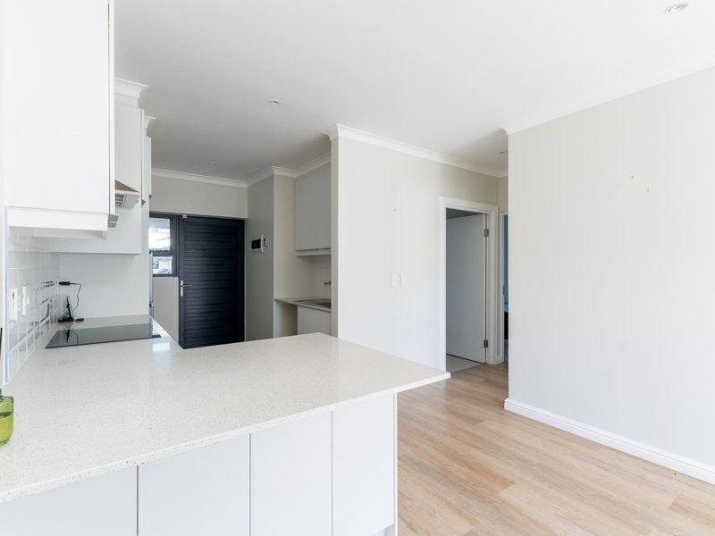 Modern open-plan kitchen featuring white cabinetry, stone countertops, and an electric hob, seamlessly flowing into the adjacent living area with light laminate flooring.