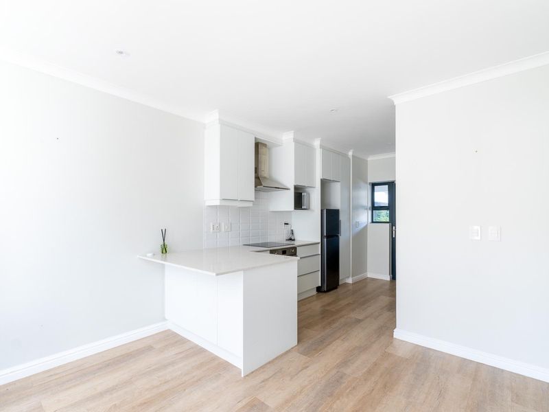 Modern open-plan kitchen featuring white cabinetry, stone countertops, integrated appliances, and light wood-look laminate flooring in a bright, minimalist space.