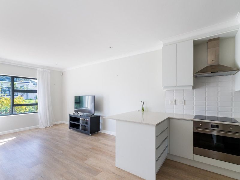 Modern open-plan living area featuring a sleek kitchen with stone countertops, built-in appliances, and light laminate flooring, flowing into a bright lounge space.