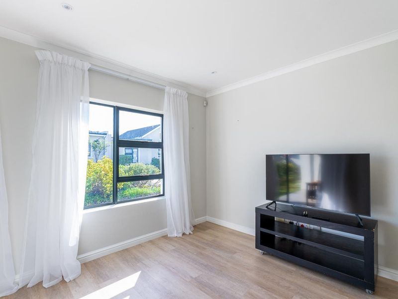 A bright living room featuring light-toned laminate flooring, neutral walls, and a large window with natural light, creating a clean and inviting atmosphere.