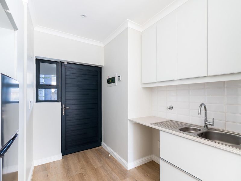 A clean and modern laundry area featuring white cabinetry, a stainless steel sink, tiled backsplash, and durable laminate flooring.