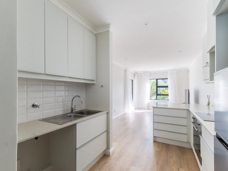Modern open-plan kitchen and living area featuring sleek white cabinetry, stone countertops, subway tile backsplash, and light wood-look flooring in a bright, neutral space.