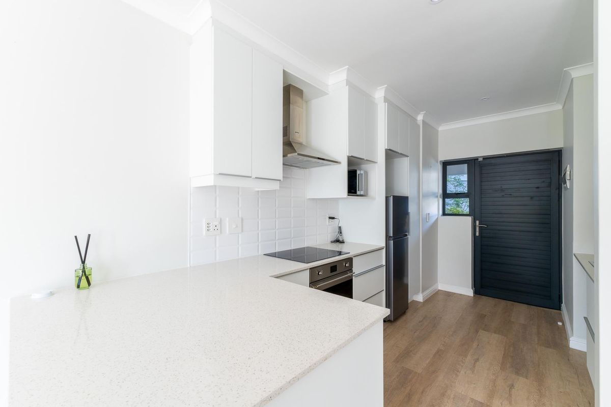 Modern kitchen featuring white cabinetry, stone countertops, built-in oven, electric cooktop, and a tiled backsplash with durable laminate flooring.