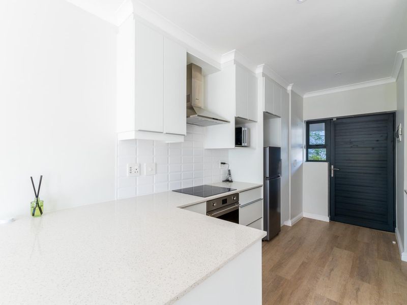 Modern kitchen featuring white cabinetry, stone countertops, built-in oven, electric cooktop, and a tiled backsplash with durable laminate flooring.