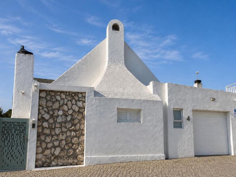 Front facade of a white-painted house featuring a prominent chimney, stone cladding detail, a garage, and a cobblestone driveway.