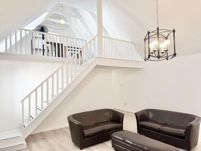Spacious living area featuring a vaulted ceiling with exposed rafters, a mezzanine level, and a timber staircase with matching balustrade.