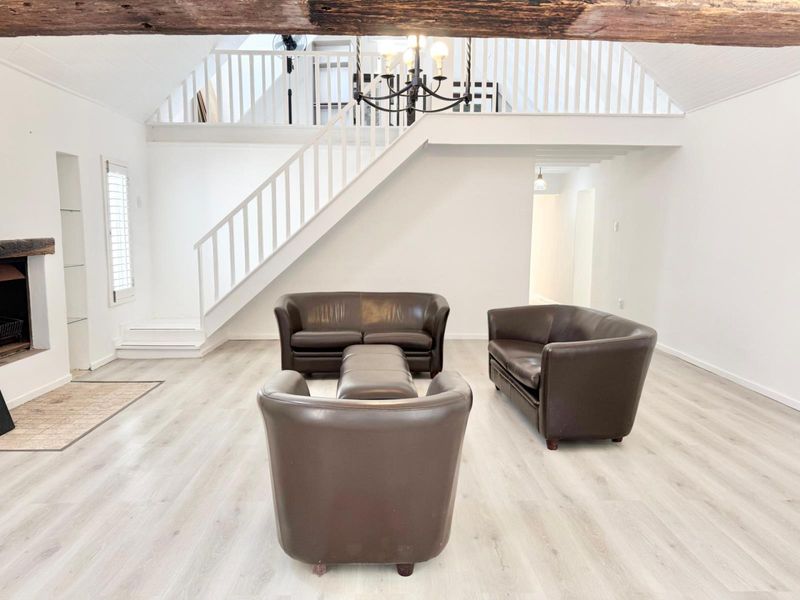 Spacious living room featuring a mezzanine level, timber staircase, exposed ceiling beam, and a fireplace with a rustic timber mantelpiece.