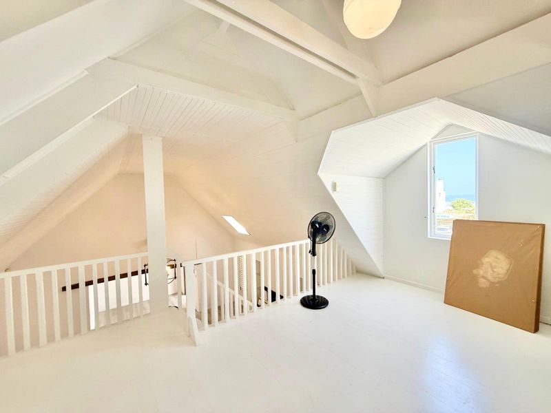 Spacious attic-style bedroom featuring vaulted ceilings, exposed timber beams, a protective balustrade, and a dormer window with coastal views.
