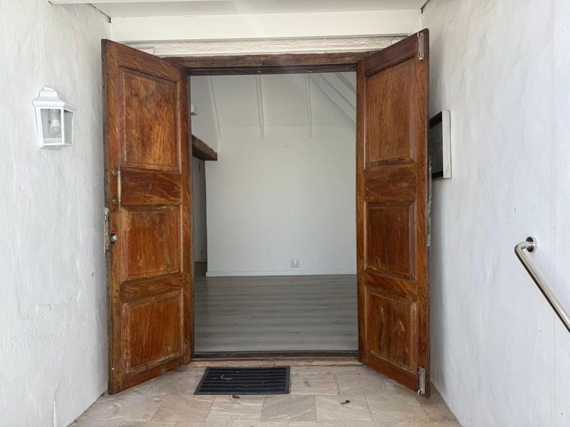 Entrance featuring double timber doors opening into a bright, empty interior space with light-toned laminate flooring and vaulted ceilings.