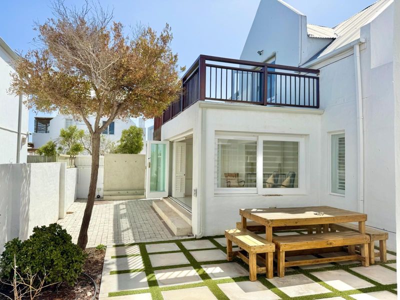 Rear exterior view featuring a paved patio area, a raised balcony with metal railing, and direct access to the interior via sliding glass doors.