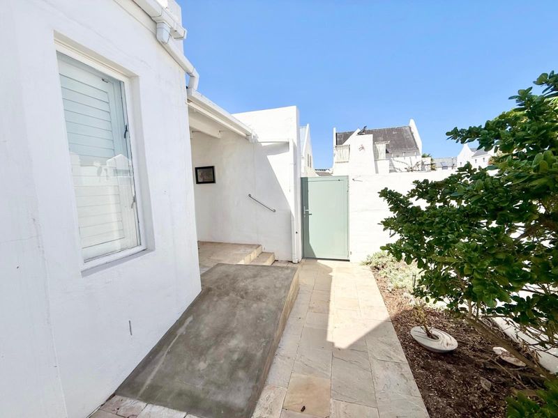 A clean rear exterior area featuring a concrete access ramp, stone paved walkway, and a secure metal gate leading to the property.