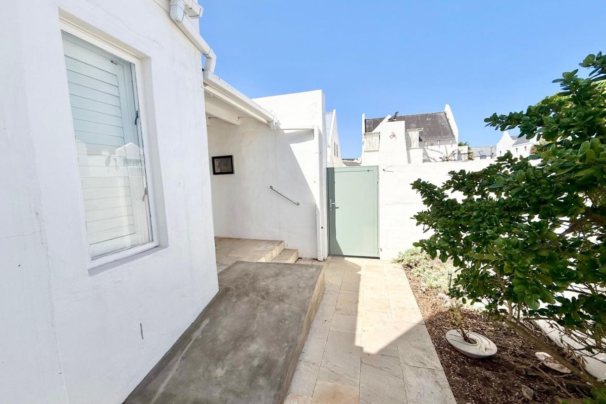 A clean rear exterior area featuring a concrete access ramp, stone paved walkway, and a secure metal gate leading to the property.