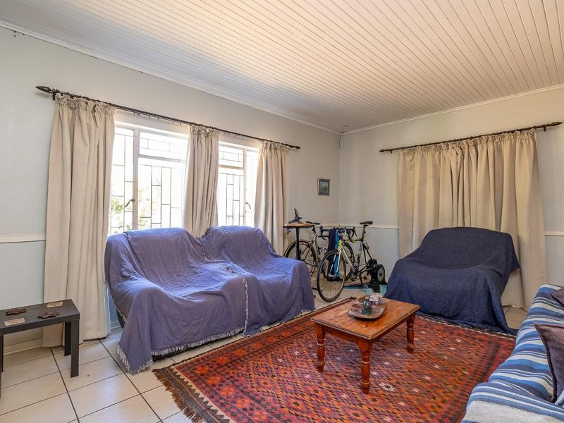 A living room featuring tiled flooring, a timber panelled ceiling, and windows fitted with security bars.