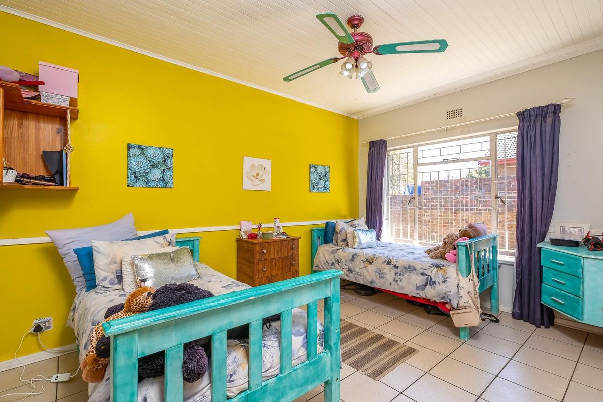 A bedroom featuring tiled flooring, a ceiling fan, and built-in shelving, with security bars installed on the window.