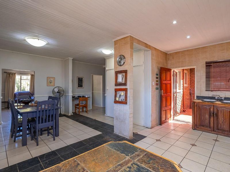 Open plan living and kitchen area featuring tiled flooring, timber ceiling paneling, and traditional wooden cabinetry with a functional sink and prep space.