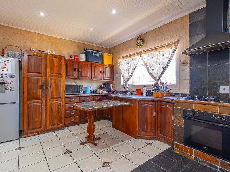 A functional kitchen featuring traditional wooden cabinetry, a built-in oven with gas hob, extractor fan, and tiled finishes throughout.