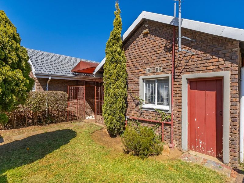 Rear view of the property featuring a face brick facade, tiled roof, and a secure entrance with a timber door.