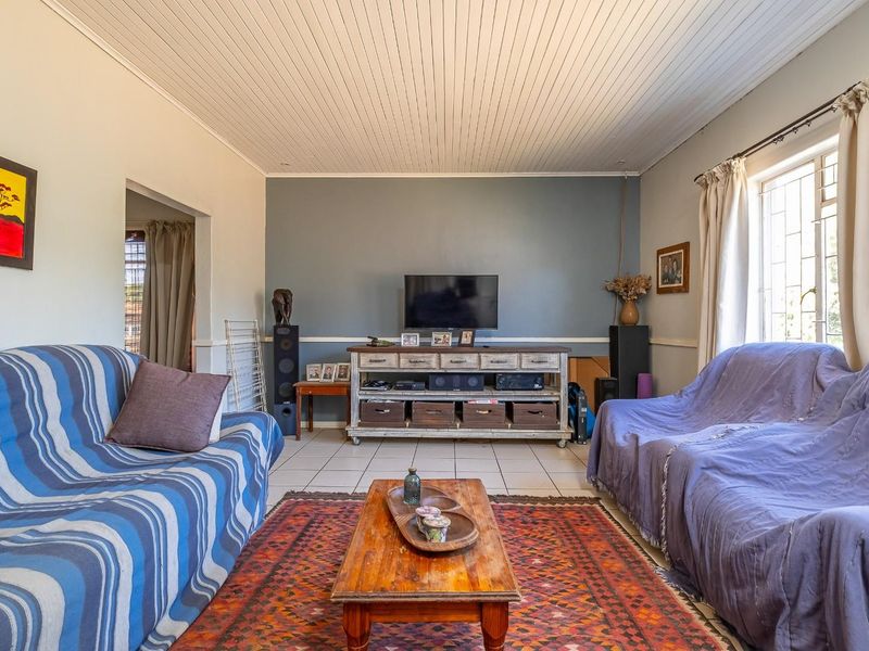 A comfortable living room featuring tiled flooring, a tongue and groove ceiling, and a large window with security bars.