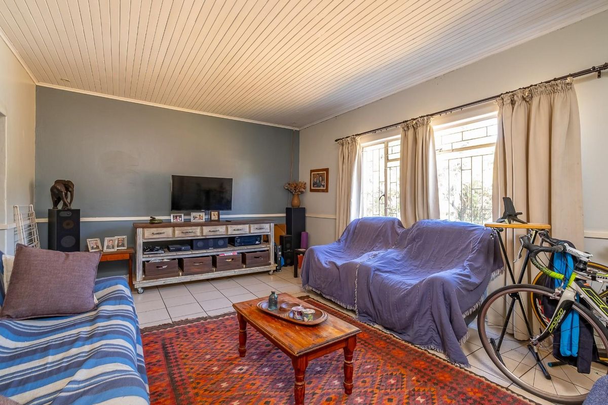 A living room featuring tiled flooring, a tongue and groove ceiling, and windows fitted with security bars.
