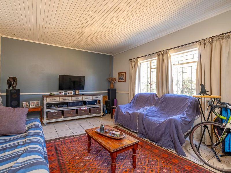 A living room featuring tiled flooring, a tongue and groove ceiling, and windows fitted with security bars.