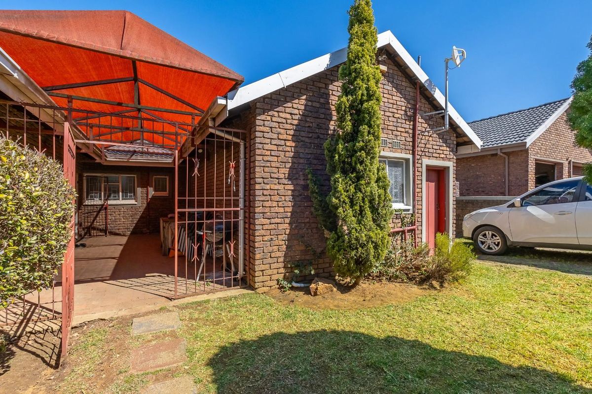 Rear view of the property featuring a face brick facade, a covered patio area with a metal security gate, and a small garden space.