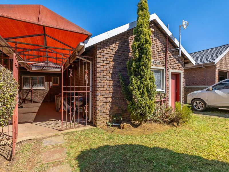 Rear view of the property featuring a face brick facade, a covered patio area with a metal security gate, and a small garden space.