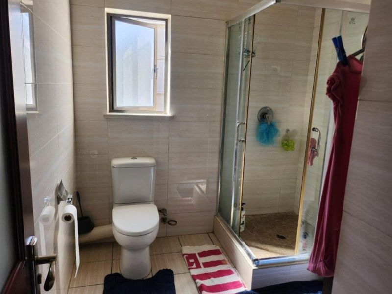 A functional bathroom featuring a glass-enclosed shower, a standard toilet, and neutral wall and floor tiling.
