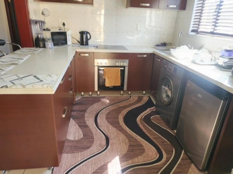 A functional kitchen featuring dark wood cabinetry, a built-in oven, electric hob, and tiled backsplash with integrated space for laundry appliances.