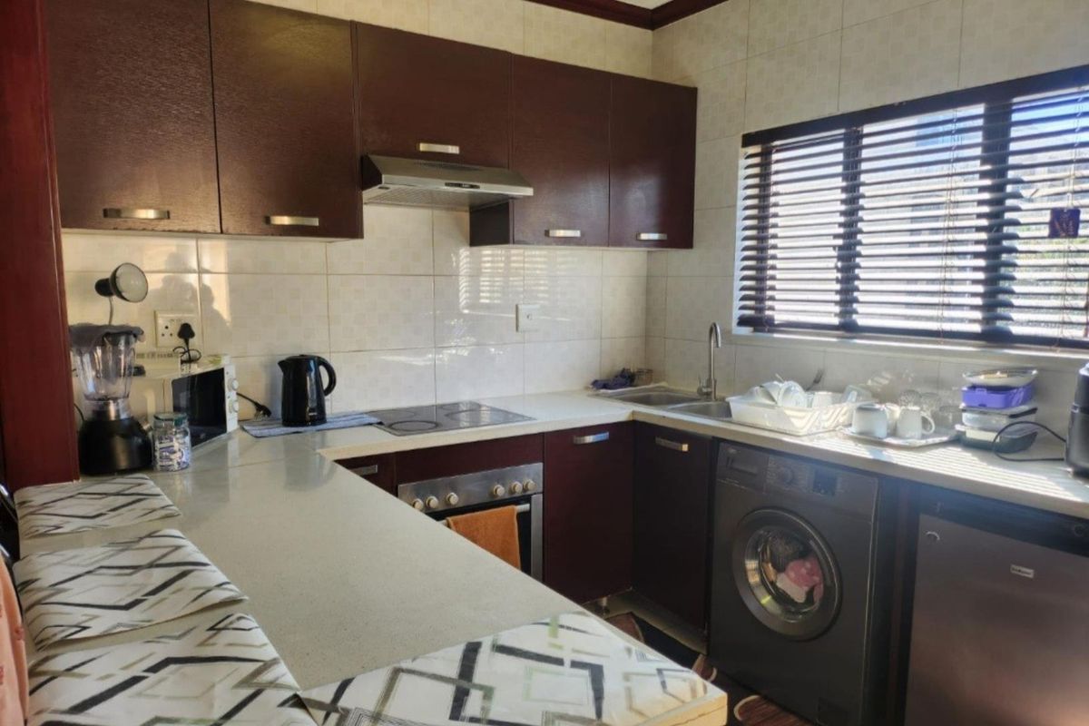 A functional kitchen featuring dark wood cabinetry, a tiled backsplash, integrated oven and hob, and a dedicated space for a washing machine.