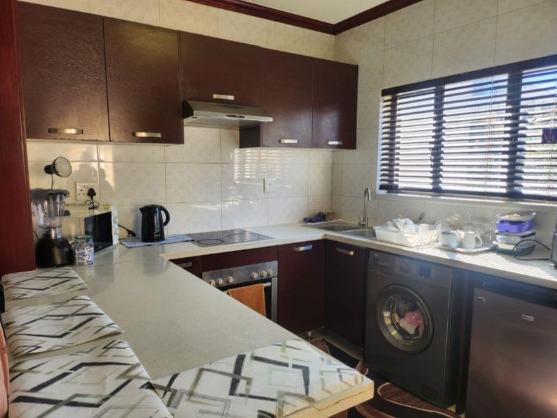 A functional kitchen featuring dark wood cabinetry, a tiled backsplash, integrated oven and hob, and a dedicated space for a washing machine.