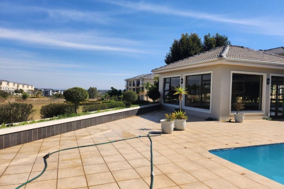 Spacious outdoor pool area featuring a tiled patio, swimming pool, and a retaining wall with views of the surrounding estate.