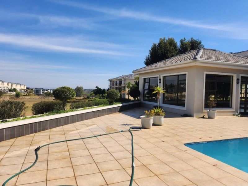 Spacious outdoor pool area featuring a tiled patio, swimming pool, and a retaining wall with views of the surrounding estate.