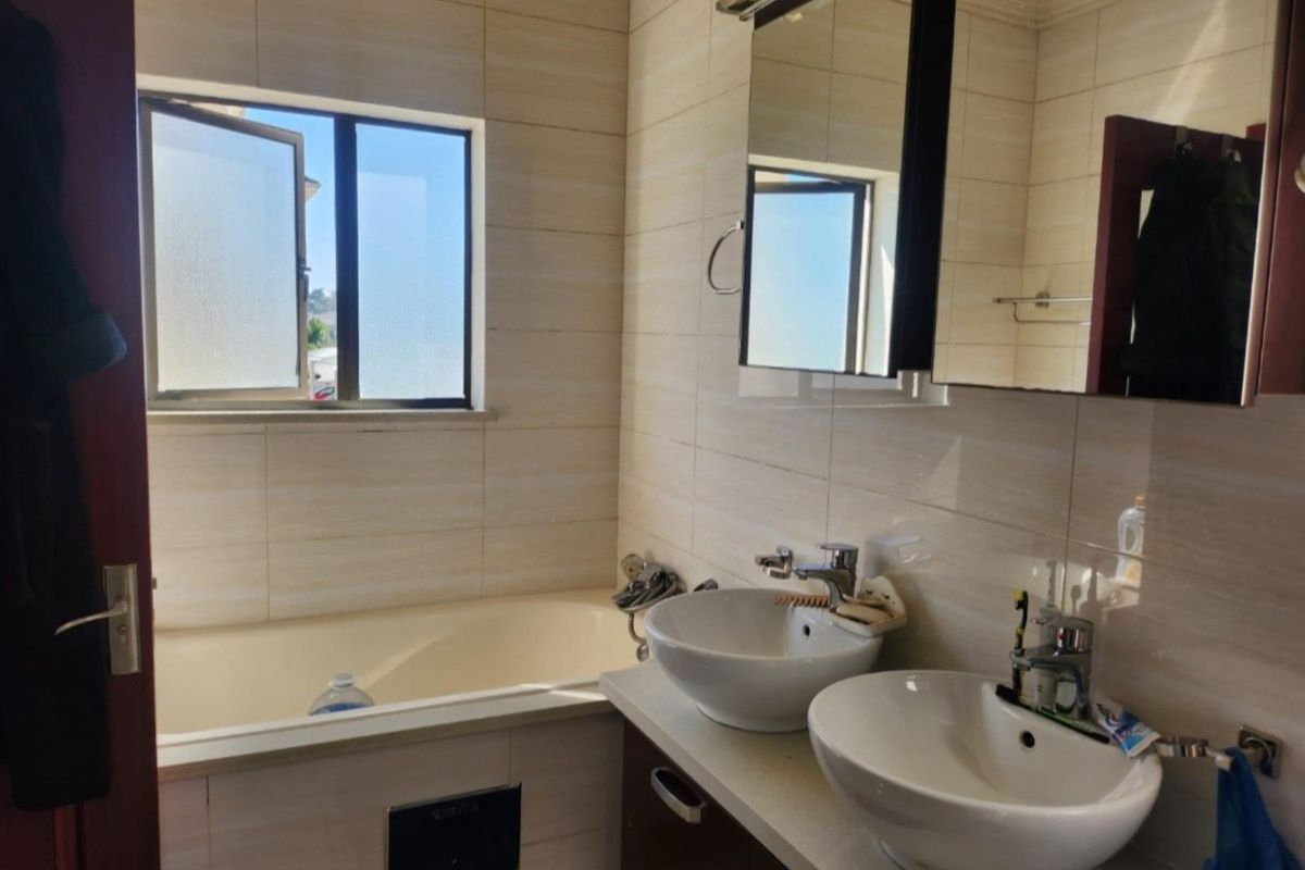 A functional bathroom featuring a double vanity with vessel sinks, a built-in bathtub, and neutral wall tiling.
