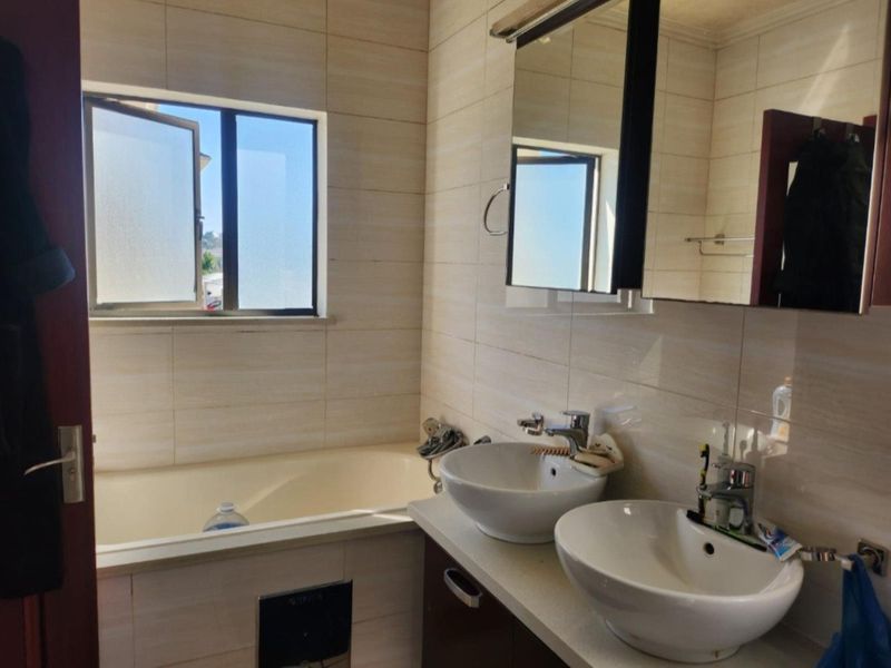 A functional bathroom featuring a double vanity with vessel sinks, a built-in bathtub, and neutral wall tiling.