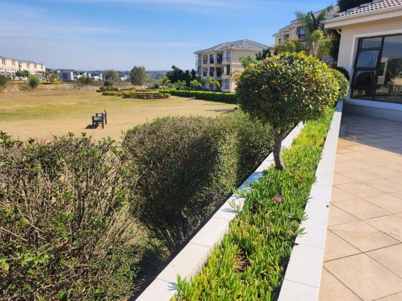 A spacious tiled balcony featuring a built-in planter box, offering expansive views over the landscaped communal gardens and surrounding apartment complex.